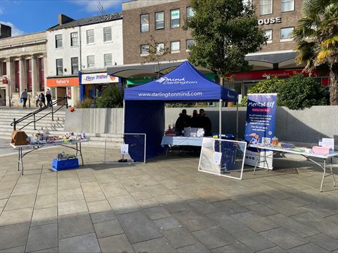 Photograph of an outdoor mental health awareness booth set up under a blue canopy labeled "Darlington Mind"
