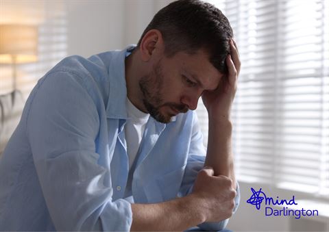 Photograph of a man sitting indoors with his head resting on one hand, appearing distressed or contemplative.