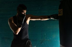 Photograph of a person wearing black boxing gloves and athletic clothing practicing a punch on a black punching bag