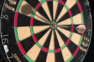 Photograph of a dartboard with a dart hitting the bullseye, highlighting precision and accuracy in the game of darts.
