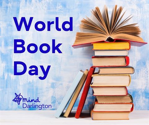 Photograph featuring a stack of books with one open book fanned out on top, set against a blue textured background. Text "World Book Day" appears in bold blue letters on the left, accompanied by a small "mind Darlington" logo at the bottom left.