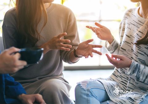 Photograph of three people engaged in a conversation, focusing on their hand gestures and casual clothing.